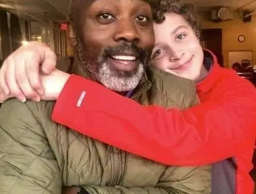 Smiling boy hugging his foster father warmly in a café setting.