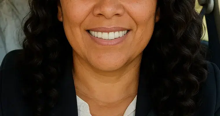 Confident woman smiling while seated in a car, wearing a dark blazer and seatbelt.