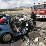 Wrecked blue car on a highway after a deadly crash, with firefighters and a fire truck at the scene
