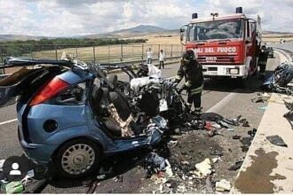 Wrecked blue car on a highway after a deadly crash, with firefighters and a fire truck at the scene