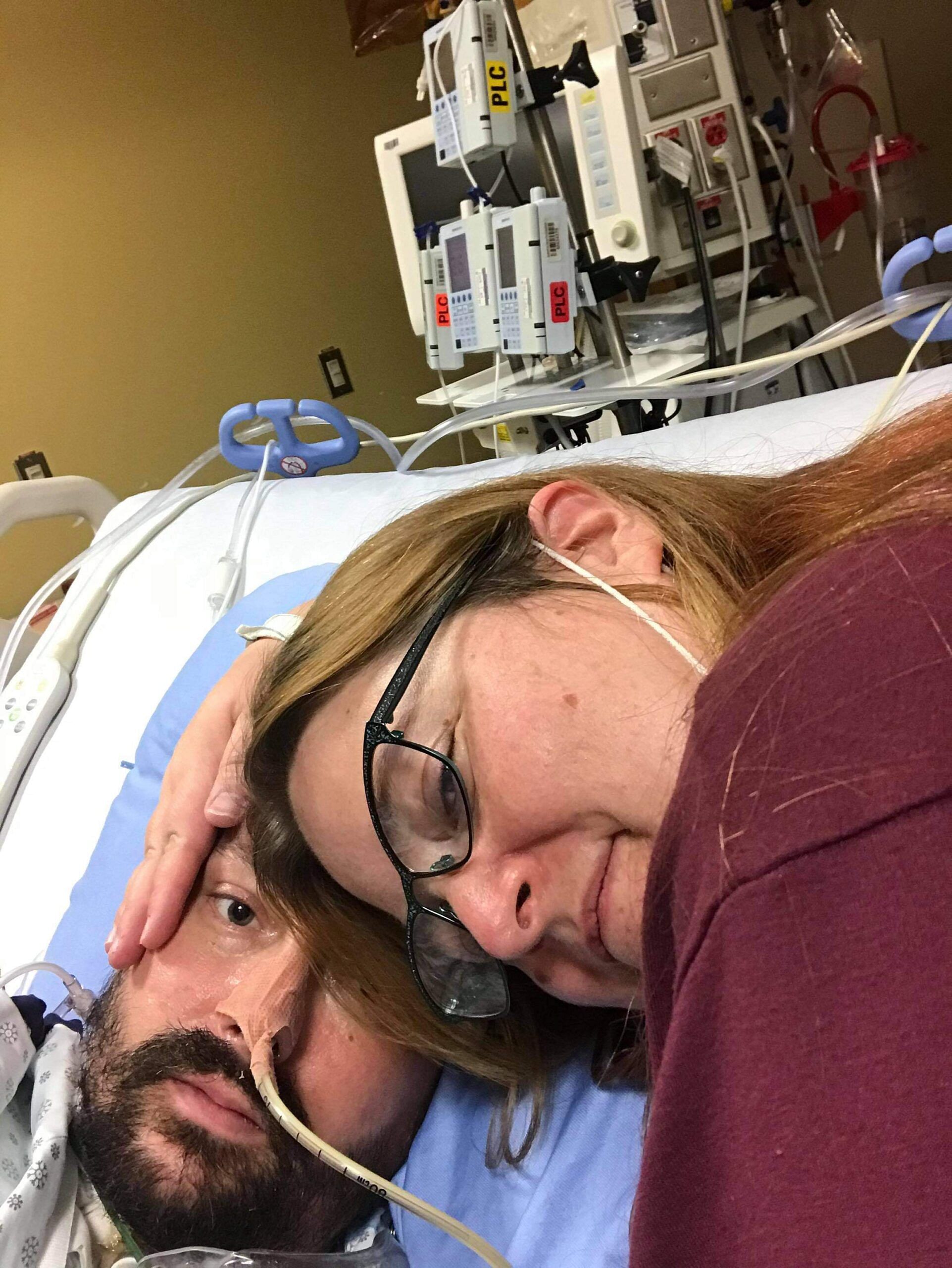 A woman lying beside her husband in a hospital bed, holding his face gently.