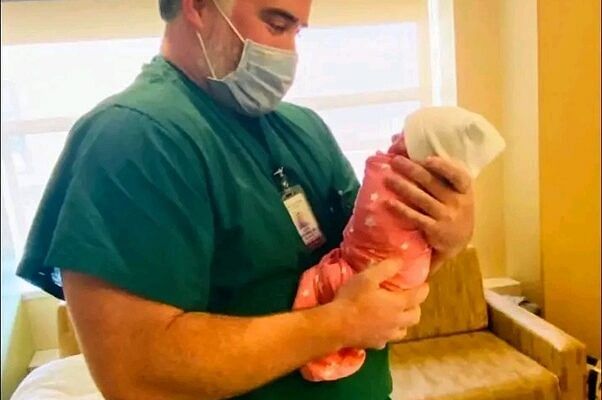 Doctor gently holding a newborn baby in a hospital room, symbolizing care and hope.