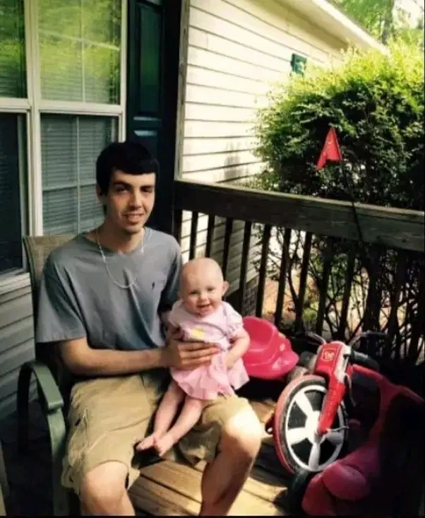 Young man sitting on a porch, holding a smiling baby on his lap.